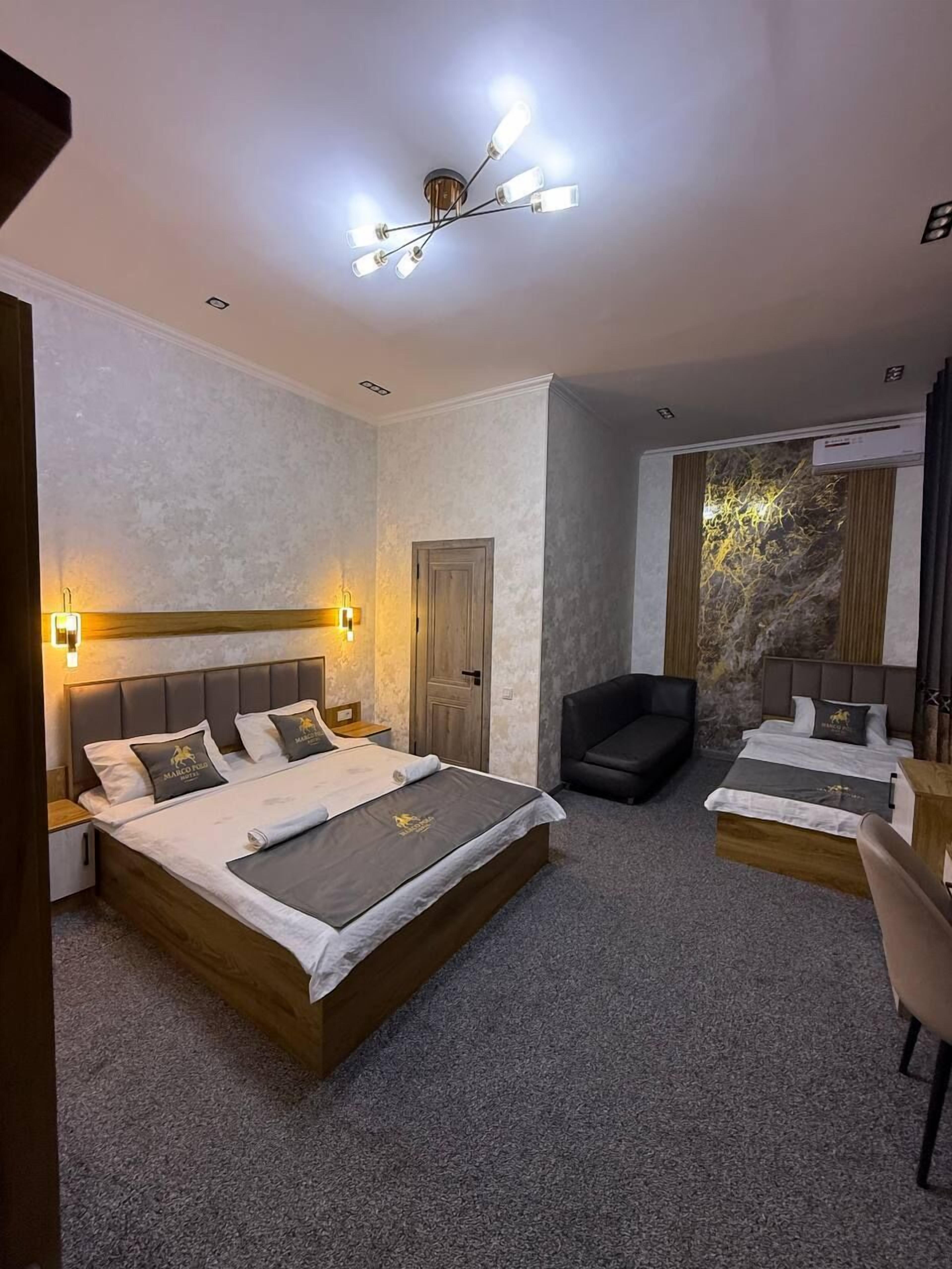 Quarto de hotel com uma cama grande, uma escrivaninha, uma cadeira e um detalhe de parede em pedra.