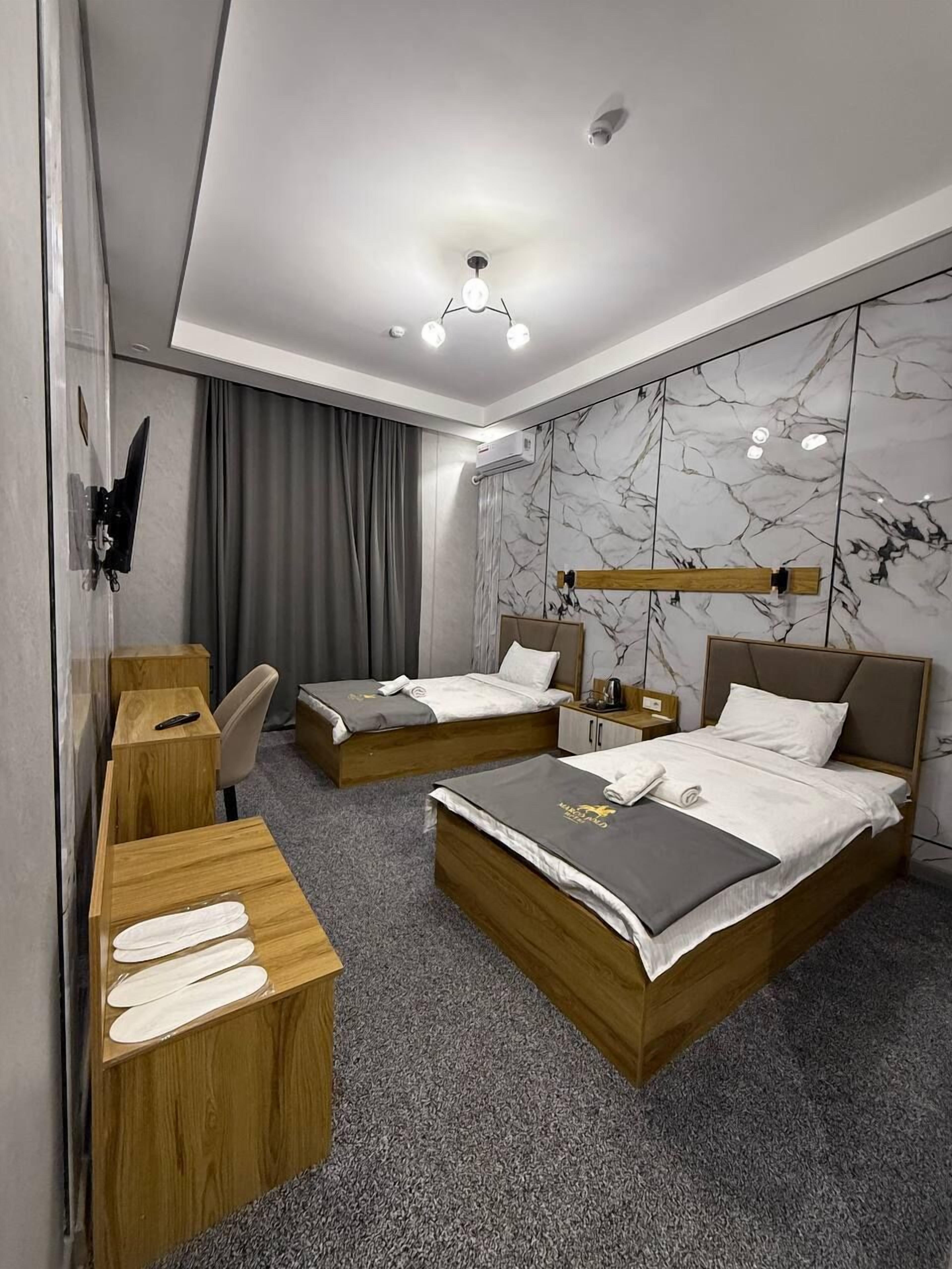 Quarto de hotel com duas camas, uma escrivaninha, uma cadeira, um guarda-roupa e parede com padrão marmorizado.
