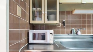 A kitchen with a microwave, stainless steel sink, and cabinets with dishes. - Skyview Serenity Duplex Shinjuku (Tokyo)