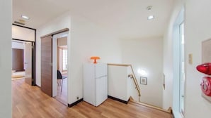 A hallway with wooden flooring, a white refrigerator, and a door with a wooden frame. - Skyview Serenity Duplex Shinjuku (Tokyo)