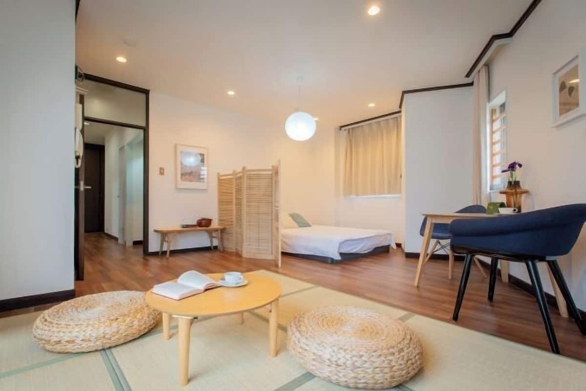 A compact room with a bed, a small table, a chair, and a sofa.