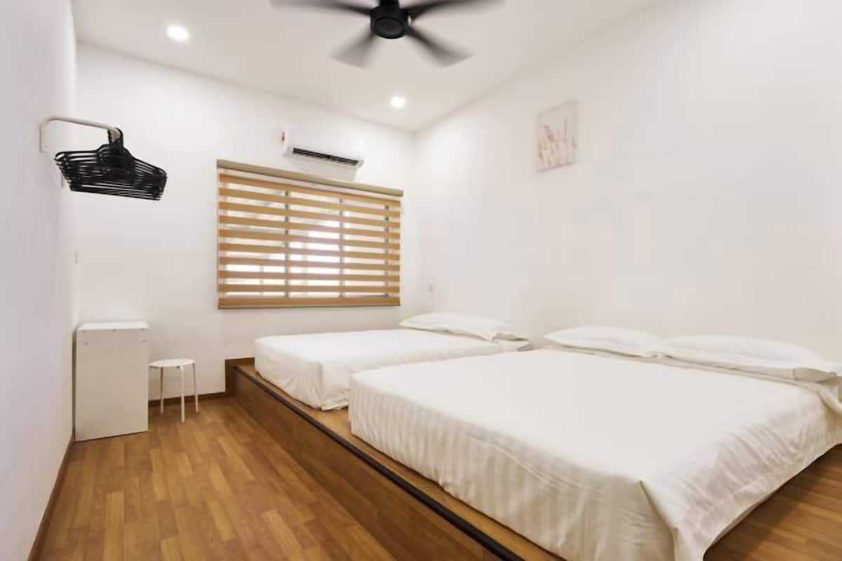 A room with two beds, a ceiling fan, a wall-mounted air conditioner, a small table, and a window with blinds.