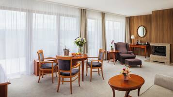 A hotel room with a dining area, a sofa, a fireplace, and a large window with sheer curtains.