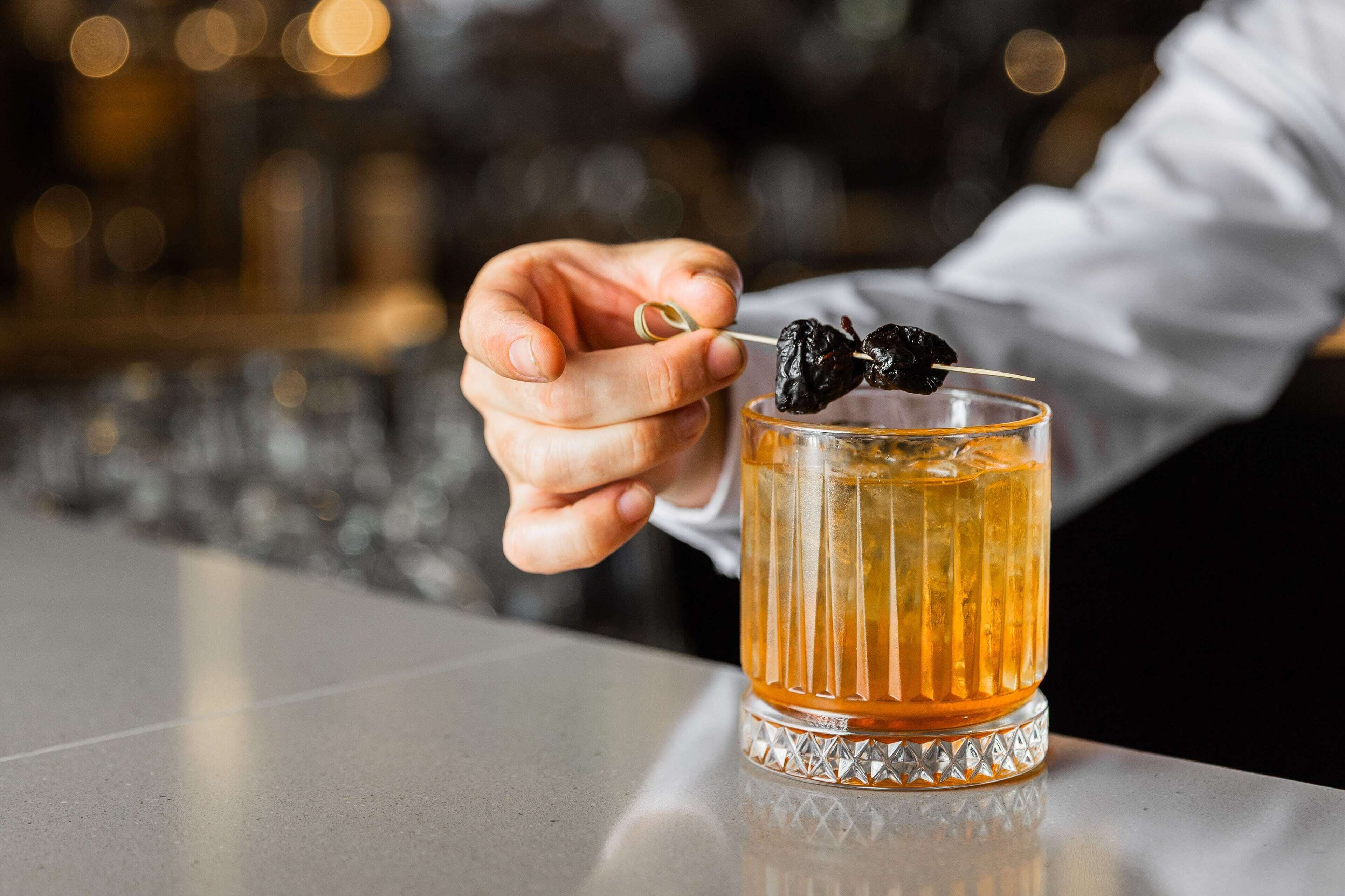 Eine Hand hält einen Cocktail mit Kirsche, platziert auf einer Theke.