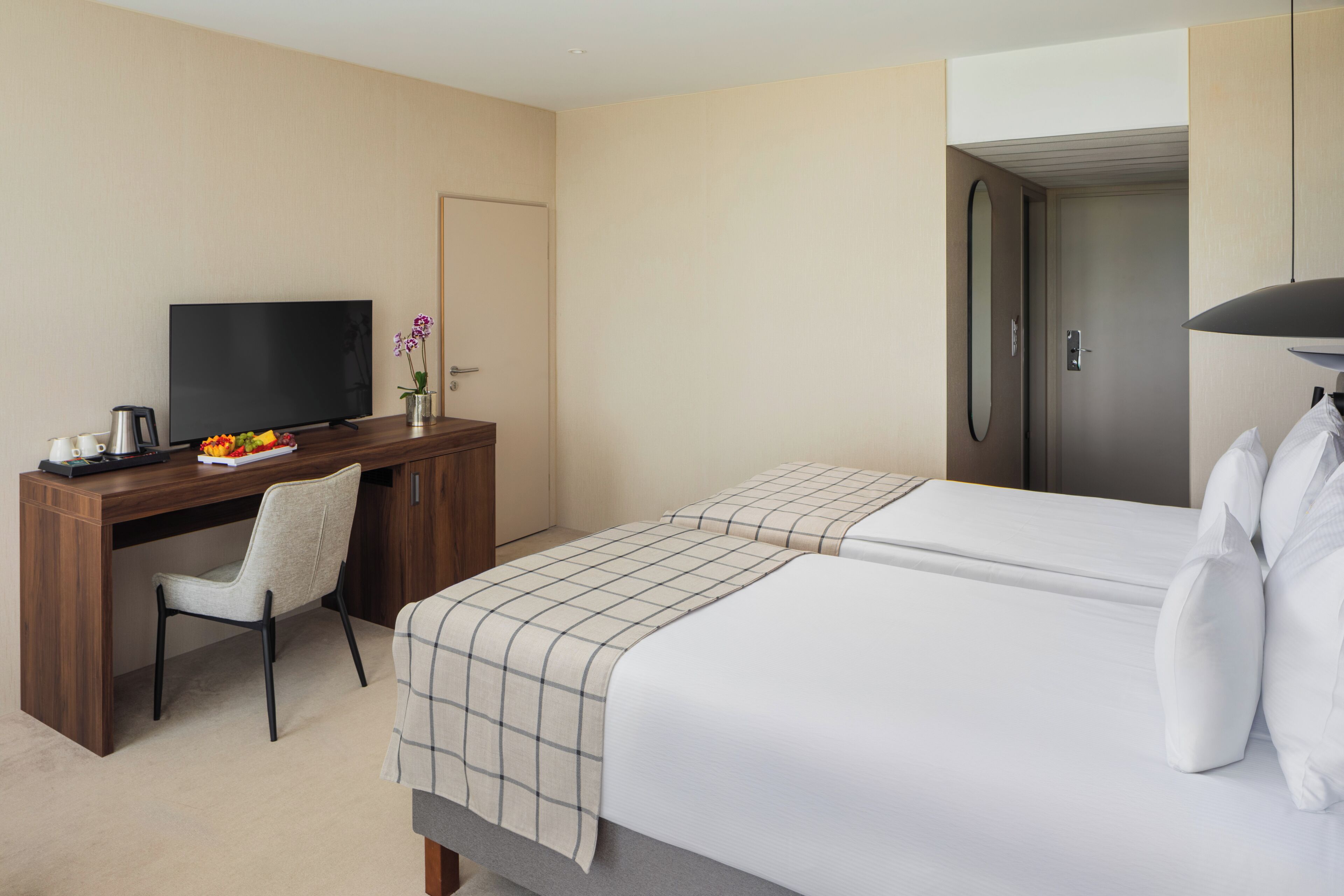 A hotel room with a bed, a desk with a TV, a chair, and a door.