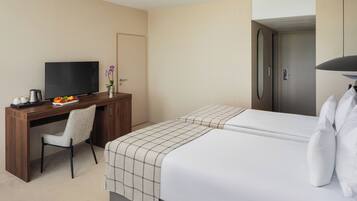 A hotel room with a bed, a desk with a TV, a chair, and a door.