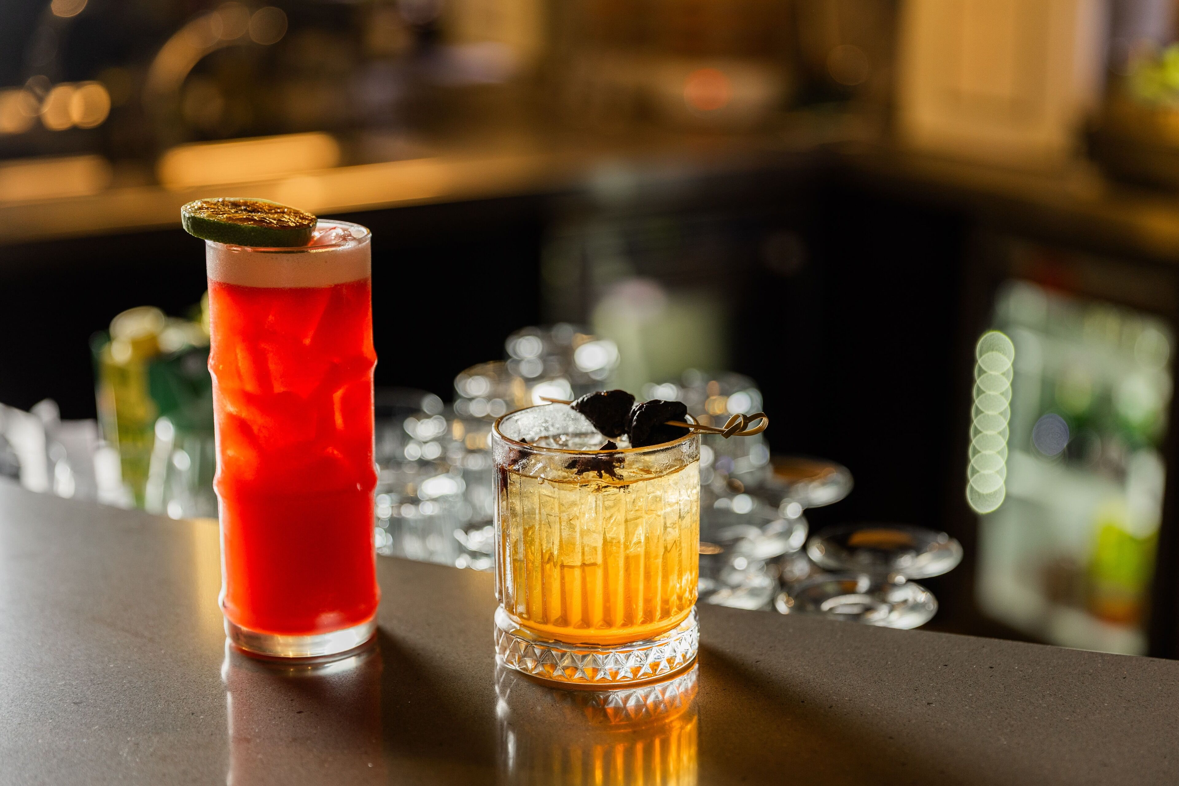 Eine Bar mit zwei Getränken, eines im hohen Glas und eines im kleinen Glas, beide mit Eis und Garnitur.