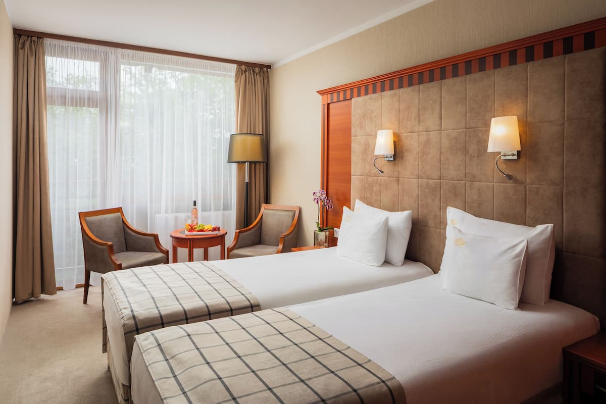 Habitación de hotel con dos camas, un área de descanso con mesa y sillas, y un ventanal con cortinas.