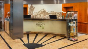 A hotel reception desk with a large welcome sign, a reception area, and a display of brochures. - Silvanus Hotel (Visegrád)