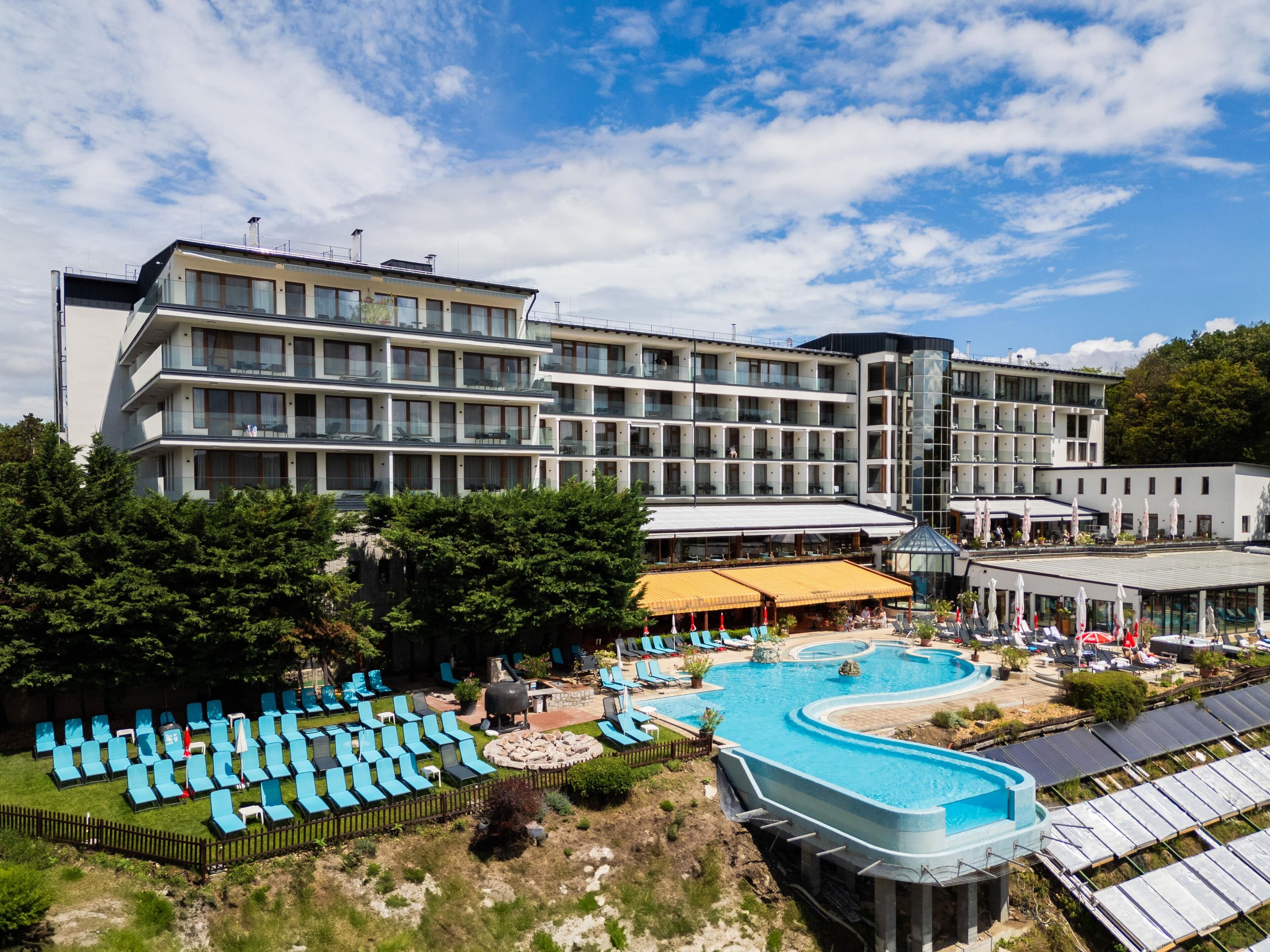 A modern hotel with multiple floors, a swimming pool, and outdoor seating areas.