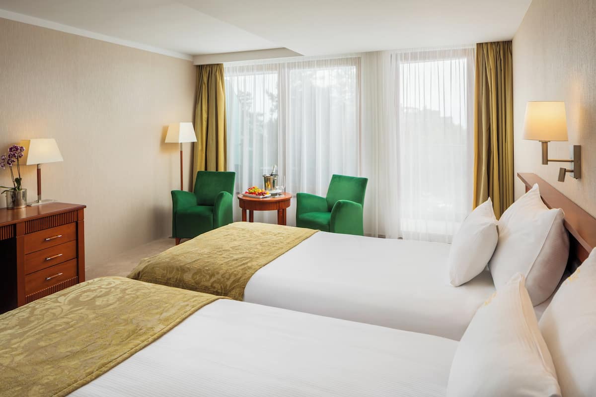 Habitación de hotel con dos camas, un escritorio, una silla, una lámpara y una ventana con cortinas.