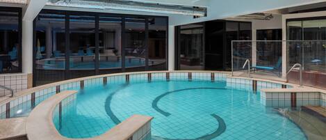 Una piscina interior de diseño curvo, rodeada de paredes de vidrio y una estructura de techo moderna.