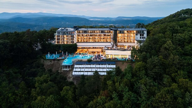 A large, multi-story hotel with a swimming pool and outdoor seating area, surrounded by forested hills. - Silvanus Hotel (Visegrád)