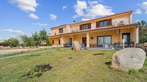 A two-story house with a patio, a stone in the foreground, and a clear blue sky. - Villa Le Torri Porto Corallo (Villaputzu)
