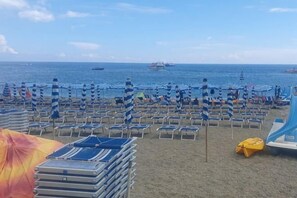 Une plage bordée de rangées de transats et de parasols, une pile de chaises longues et un radeau jaune.
