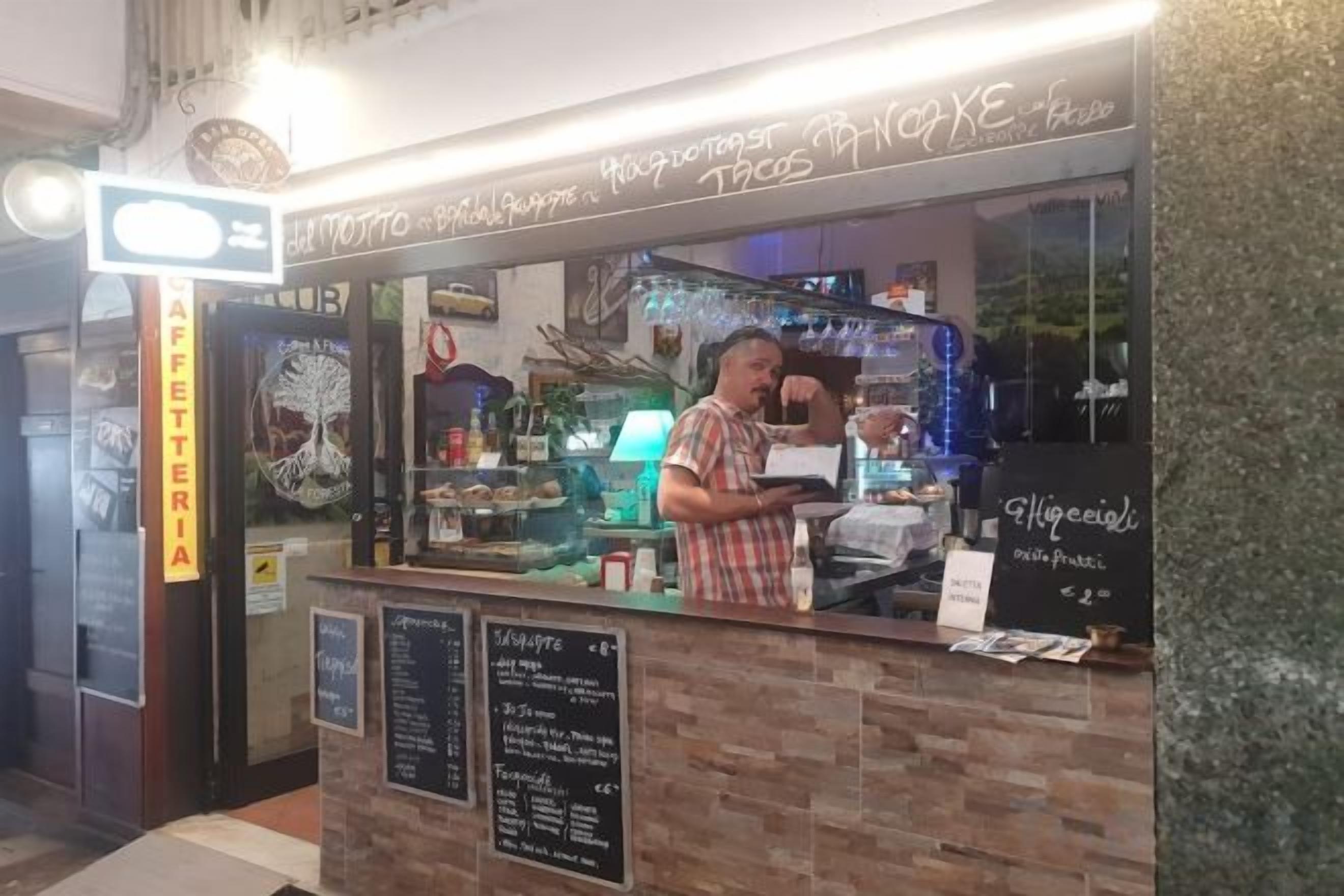 Un caffè con un bancone, una lavagna dei prezzi e una persona al servizio.