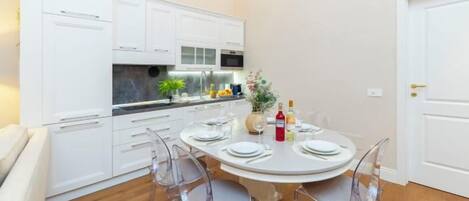 Une cuisine de taille réduite avec des meubles blancs, une table à manger avec des chaises et une porte située sur le côté droit.