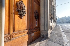 Een gevel met sierlijk houtsnijwerk, een metalen plaquette en een trottoir.