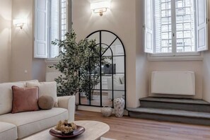 Een zithoek met een bank, een salontafel, een grote plant en een open haard.