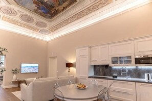 Een moderne keuken met witte kasten, een eetgedeelte met een ronde tafel, en een aan de muur bevestigde televisie.