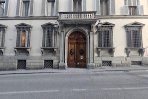 Un bâtiment doté d’une grande porte en bois, de nombreuses fenêtres avec volets et d’une façade en pierre.