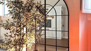 Une pièce avec une grande plante en pot, une cloison en métal noir et un meuble blanc à l’arrière-plan.