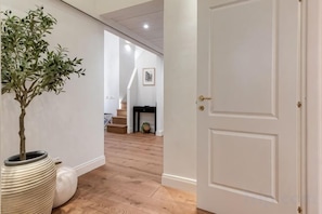 Un couloir avec un pot de fleurs, une porte blanche et un escalier en arrière-plan.