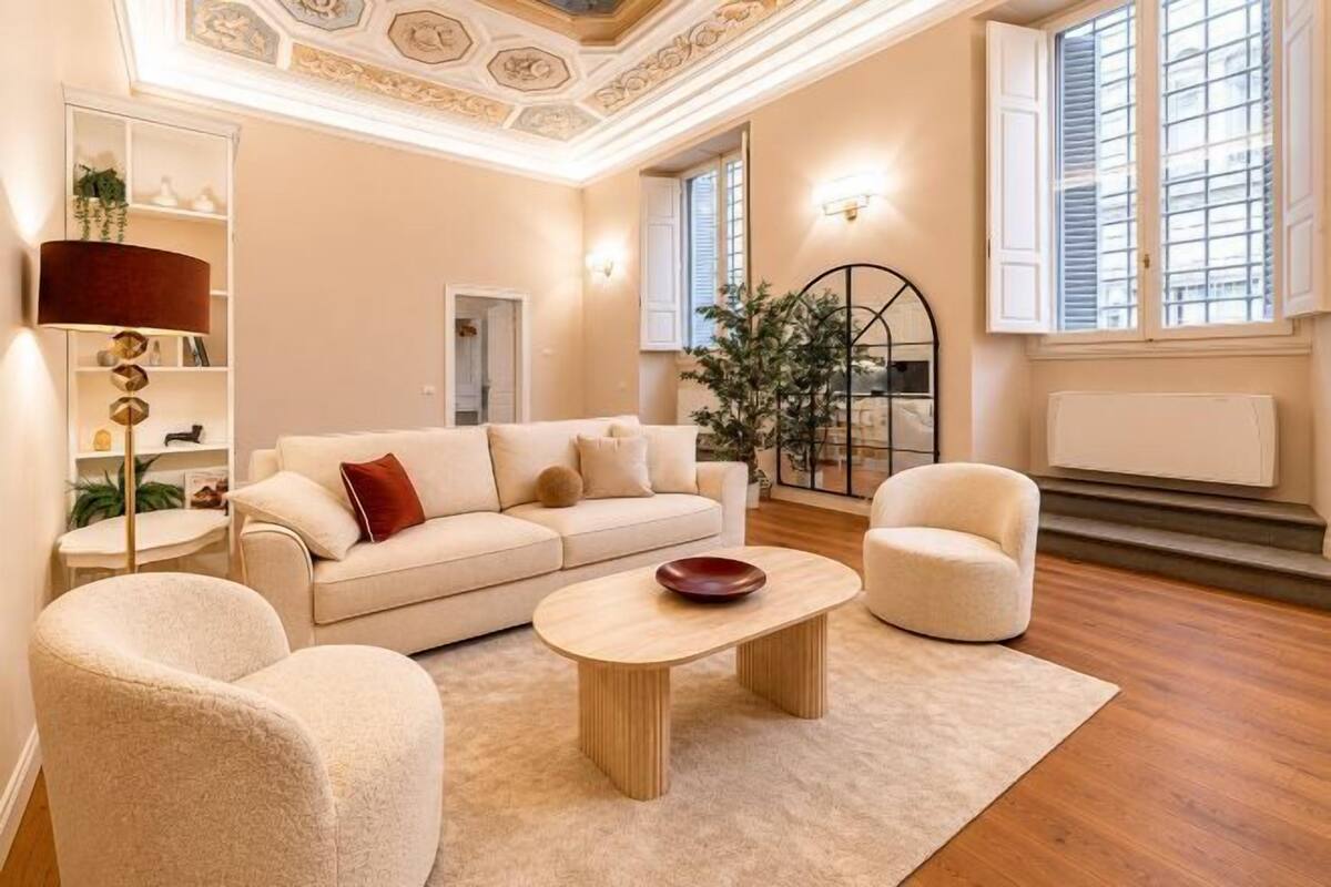 Una sala de estar con un sofá, dos sillones, una mesita de centro, una lámpara de pie y una planta.