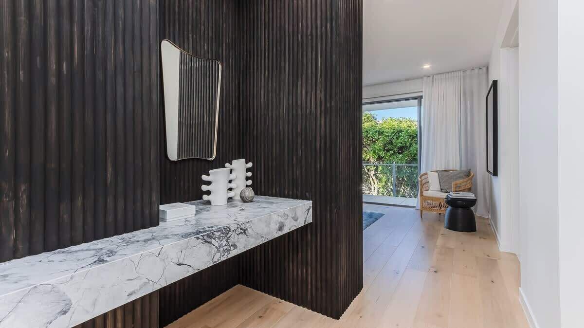 Un bagno moderno con un piano in marmo, uno specchio grande e una parete nera.