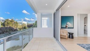 A modern balcony with a glass railing, a view of the city, and a painting on the wall.