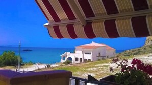 A coastal view with a red and white striped awning, a white building with a red roof, and a clear blue sky. - House Scala Dei Turchi (Realmonte)