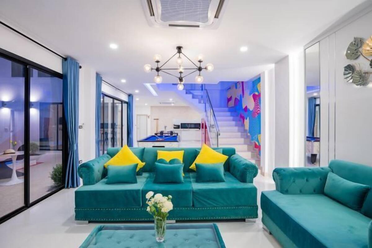 A modern living room with teal sofas, a central coffee table, and a staircase leading to a balcony.