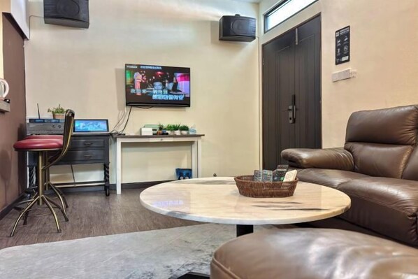 A hotel room with a leather sofa, a round table, a TV, a desk with a computer, and a small plant. - Auguri Bercham Landed 6BR Karaoke Set BBQ (Ipoh)