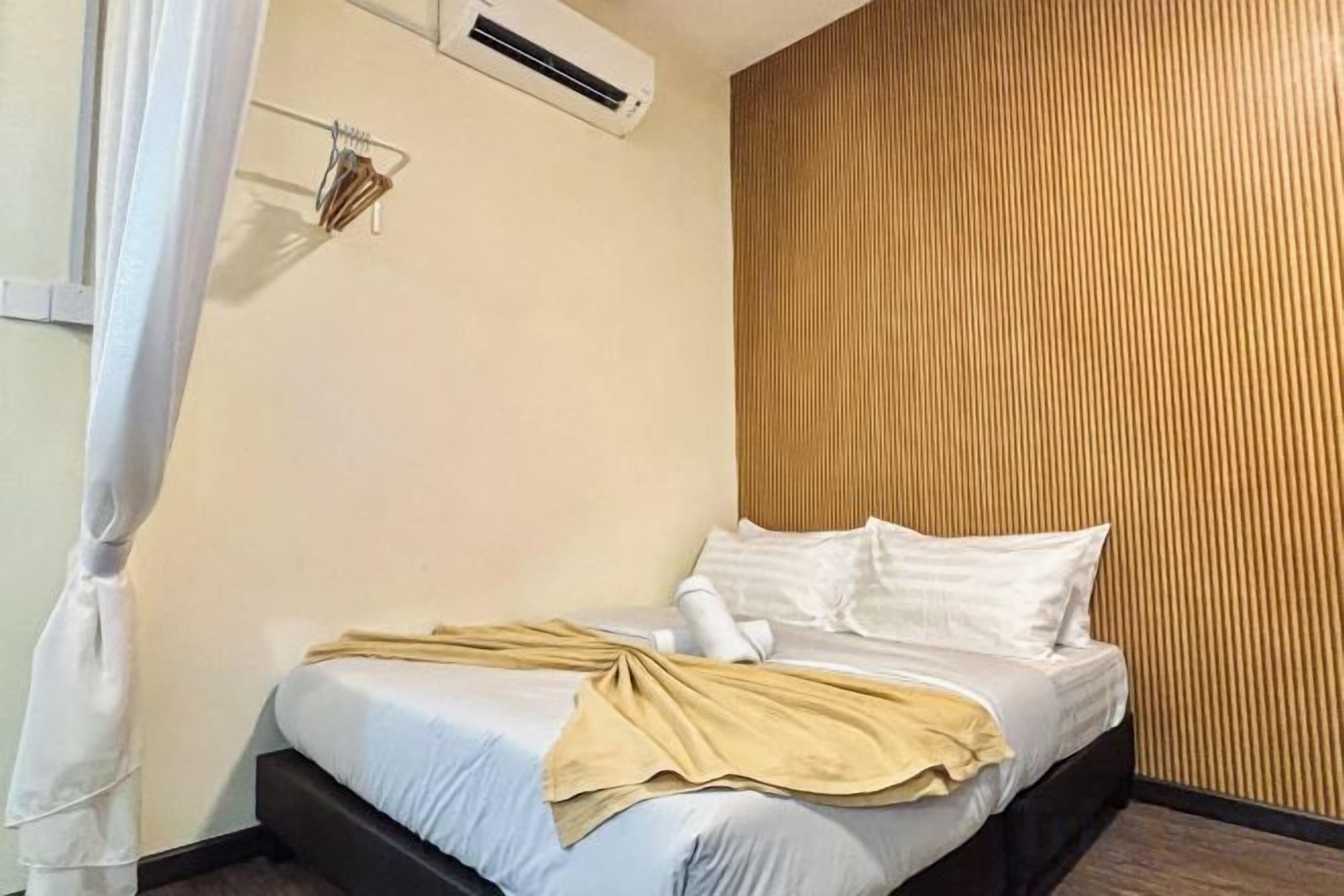 A hotel room with a bed, a wall-mounted air conditioner, and a wooden panel wall.