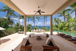 Ein überdachter Außenbereich mit Pool, Palmen und Blick auf das Meer.