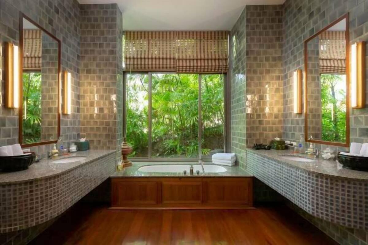 Ein Badezimmer mit zwei Waschbecken, einer großen Badewanne und Blick auf Grün durch ein Fenster.