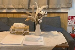 A room with a bed, a bedside table, a vase with dried flowers, a basket, and a fire extinguisher on the wall. - Zenju B (Osaka)