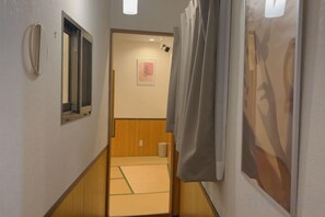 A narrow hallway with tatami mats, a wooden door, and a framed picture on the wall. - Zenju B (Osaka)