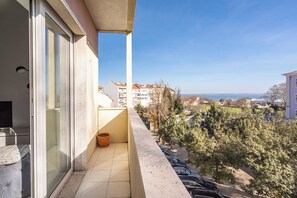 A balcony with a view of a residential area, a tiled floor, and a potted plant.