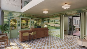 Une pièce avec un sol à carreaux, un comptoir d’accueil en bois, deux chaises, une lampe et une vue sur la cour intérieure, visible à travers une porte vitrée.