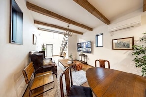 A dining area with a wooden table and chairs, a chandelier, and a staircase leading to an upper level.