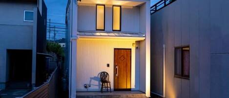 Un bâtiment moderne à deux étages, doté d’une porte d’entrée, d’un petit porche et d’une chaise à l’extérieur.
