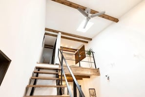 Una escalera con vigas de madera, barandilla de metal y una lámpara en el techo.