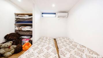A small room with a bed, a shelf with folded blankets, and an air conditioning unit.