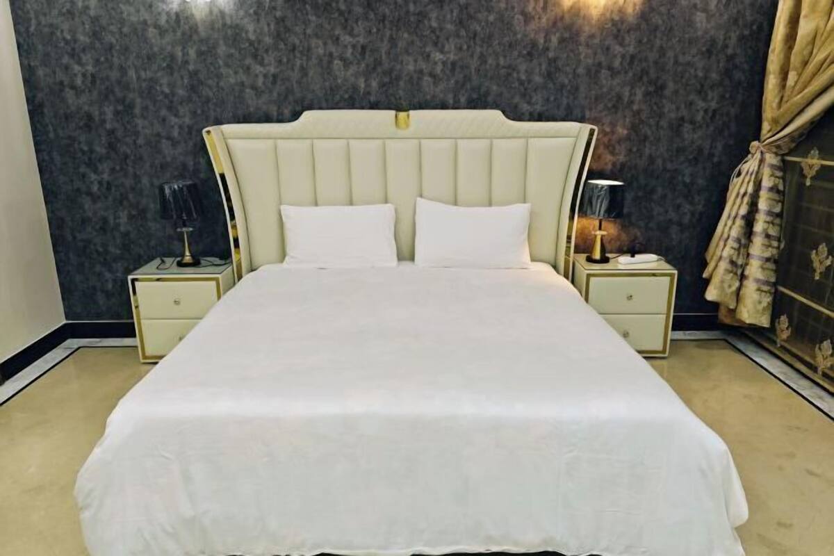 A neatly made bed with a headboard, two bedside tables with lamps, and a dark wall with a curtain.