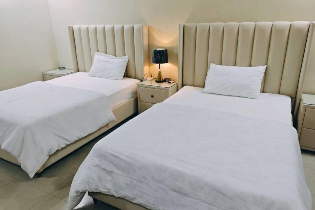 A hotel room with two beds, each with a nightstand and a lamp.