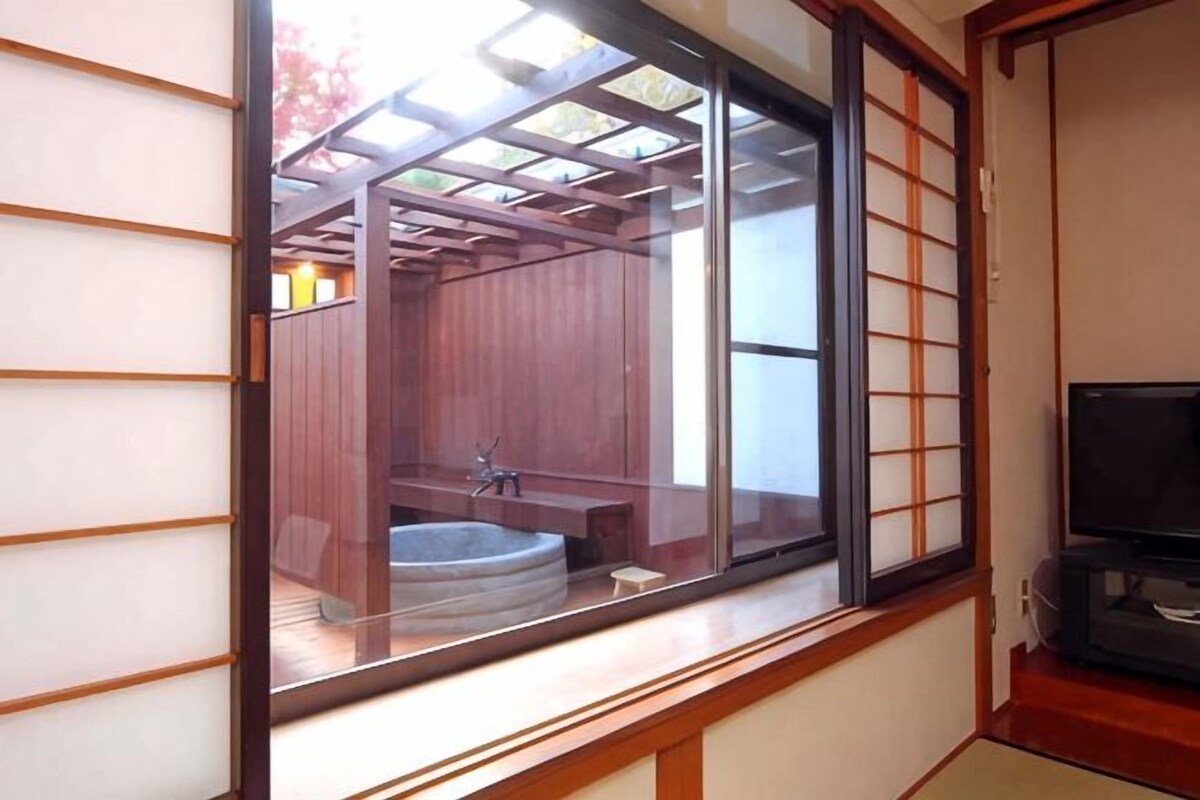 A traditional Japanese room with tatami flooring, a sliding door, and a view of a wooden sauna.