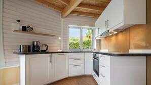 A modern kitchen with white cabinetry, a wooden ceiling, and a large window providing a view of greenery outside. - Vacation home "Kirana" on Lake Tollensesee in Penzlin Wustrow (Penzlin)