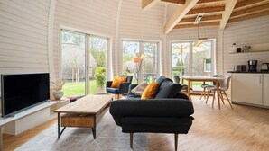 A spacious living area with a large TV, wooden coffee table, and a sofa with cushions. There is a dining table with chairs and a kitchen area with cabinets and a countertop. - Vacation home "Kirana" on Lake Tollensesee in Penzlin Wustrow (Penzlin)