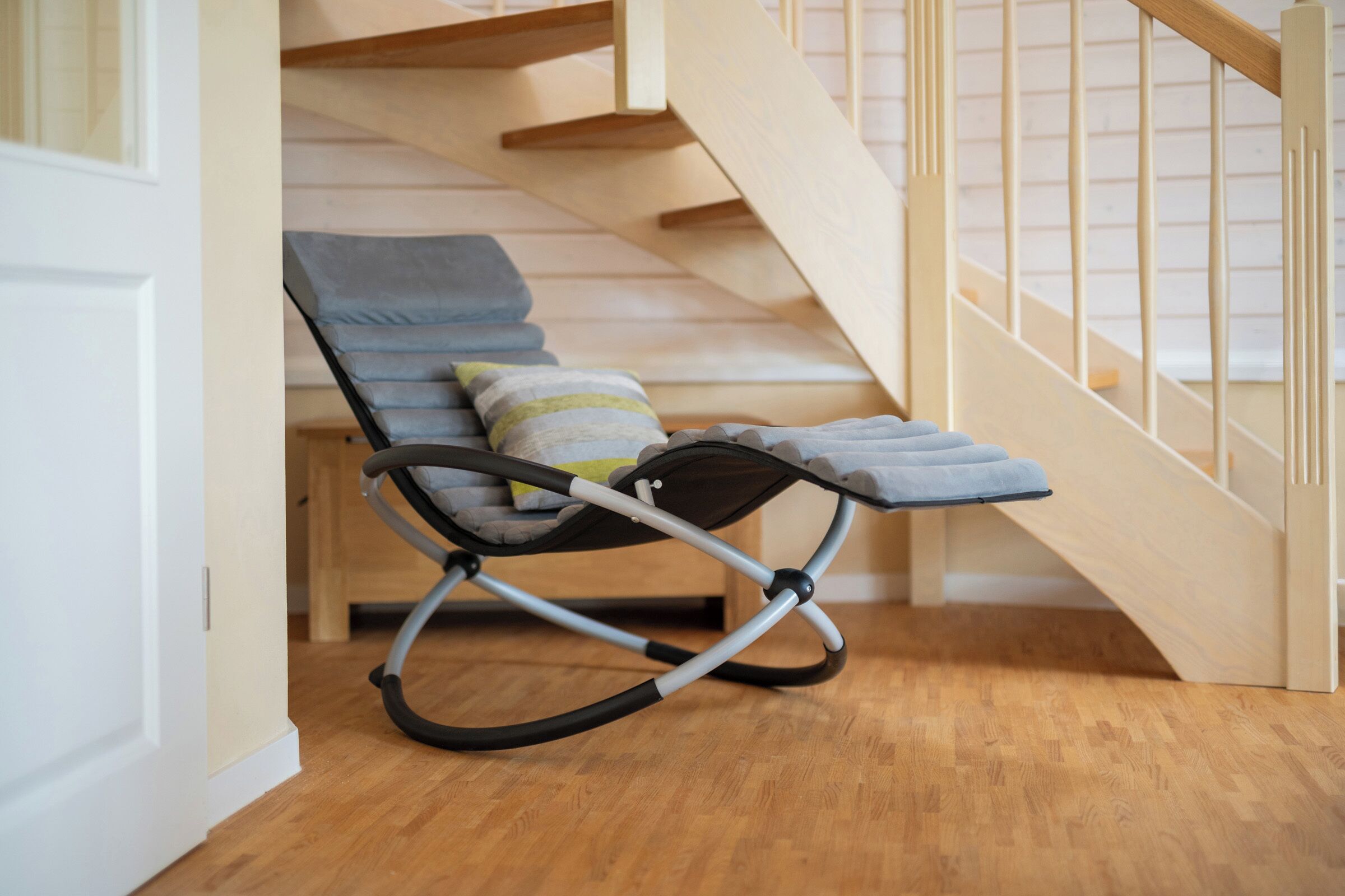A room with a wooden staircase, a rocking chair with cushions, and a wooden floor.